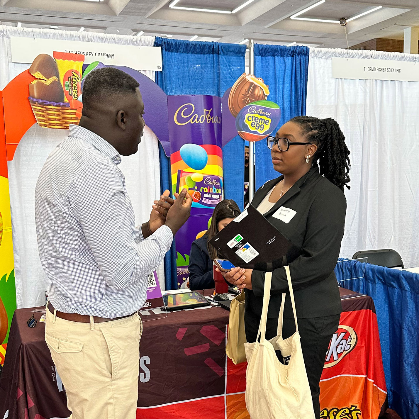 Two people speaking next to the Hershey Company booth at the career fair.