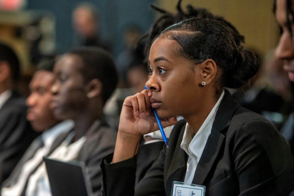 A female student in a suit listens to a lecture.